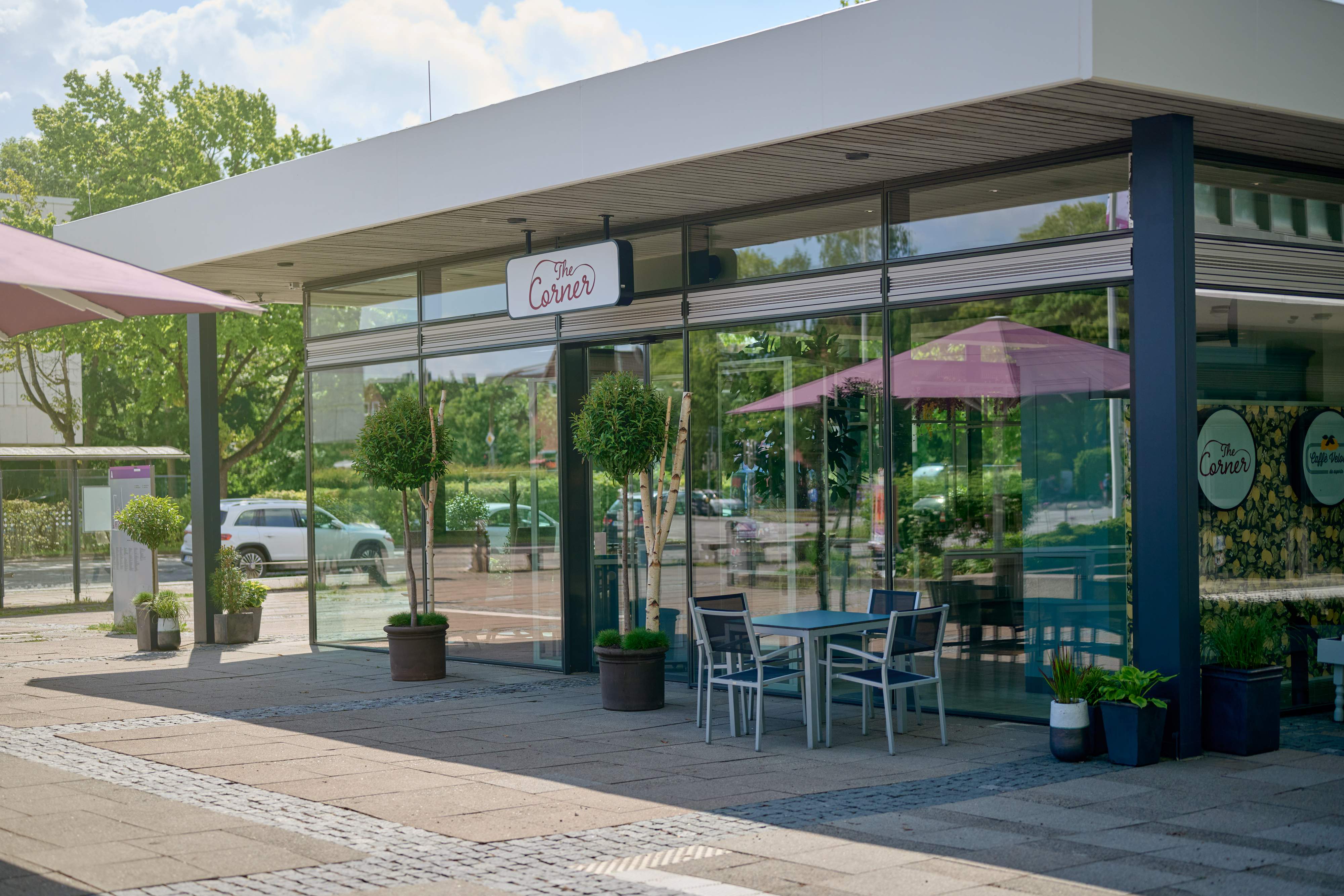 Außenansicht von The Corner mit Glasfassade und Außenbestuhlung